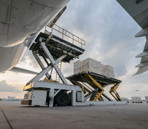 Air freight cargo being loaded onto aircraft with lift platform on airport tarmac.